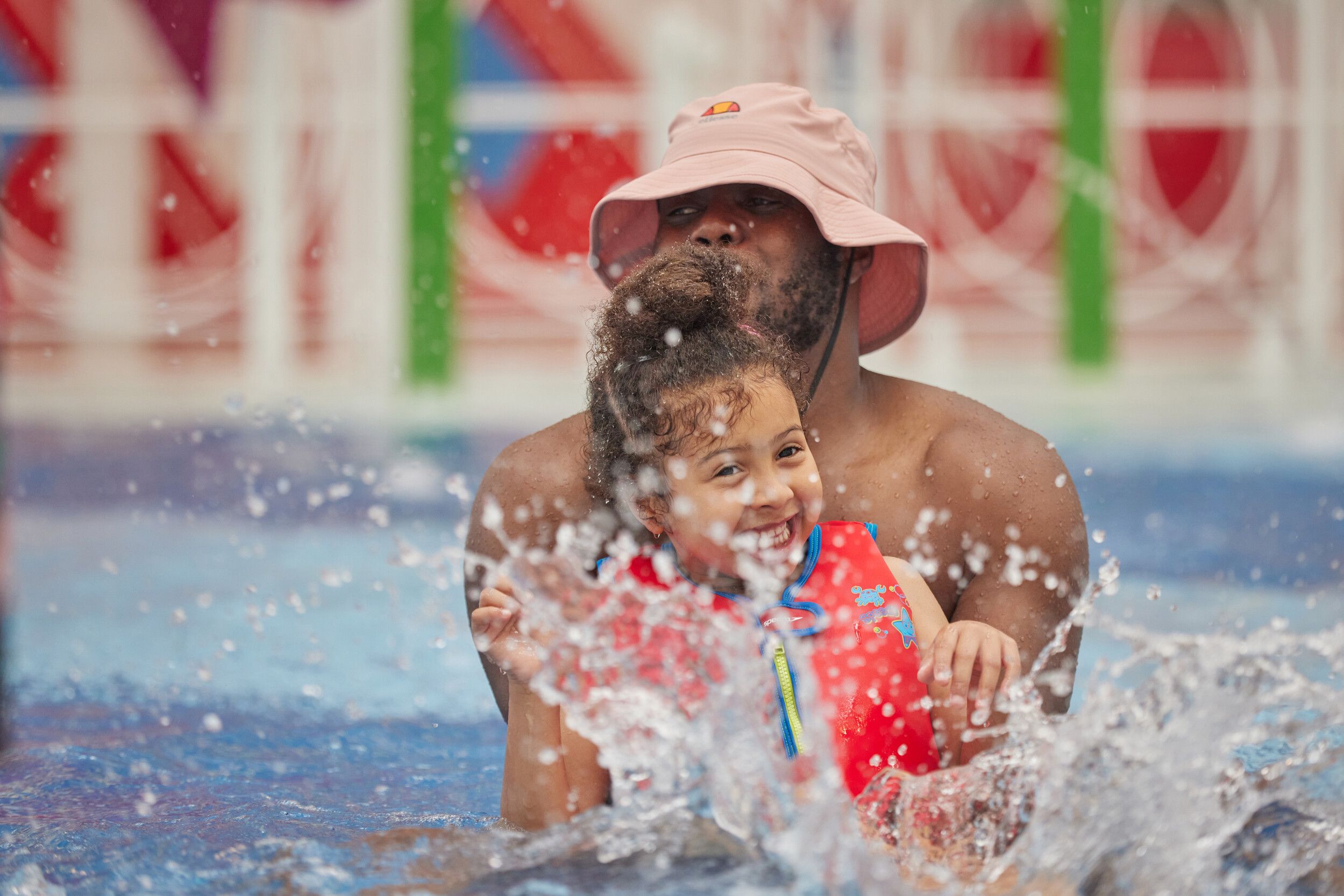 A father and his child splash together in the pool.