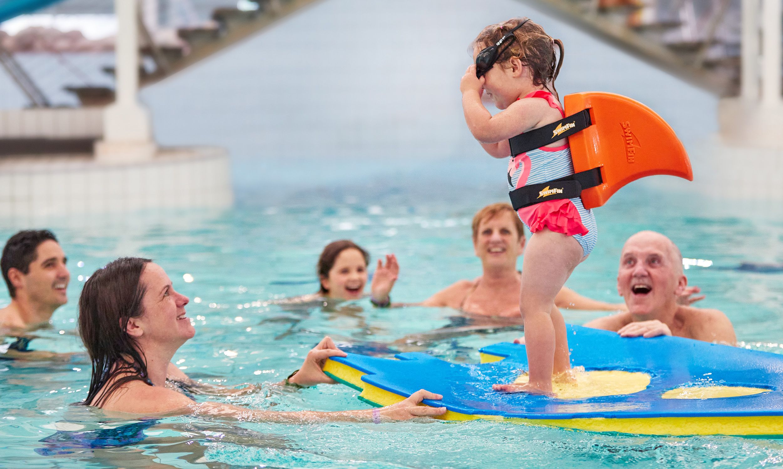 A tot plays on a float in the water while her parents look up at her.