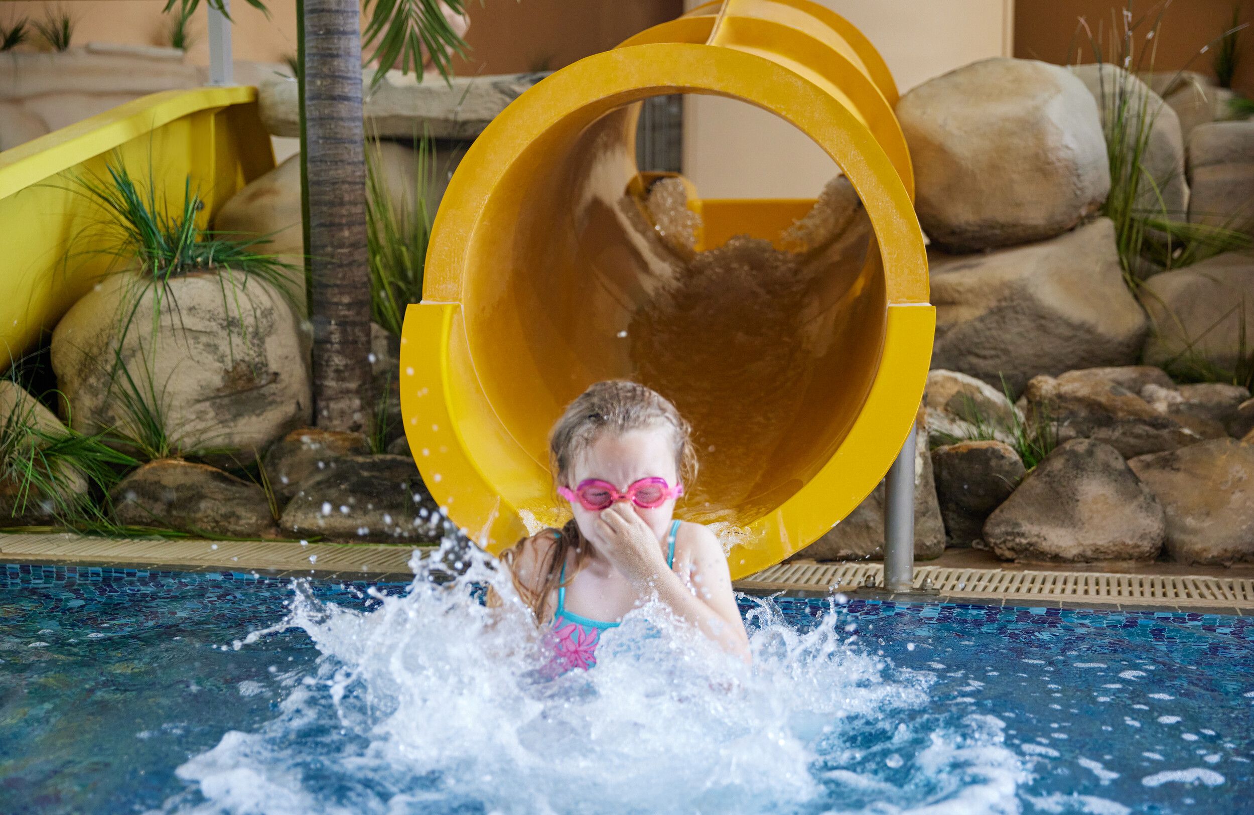 A young girl exiting a yellow slide at Skegness pool.