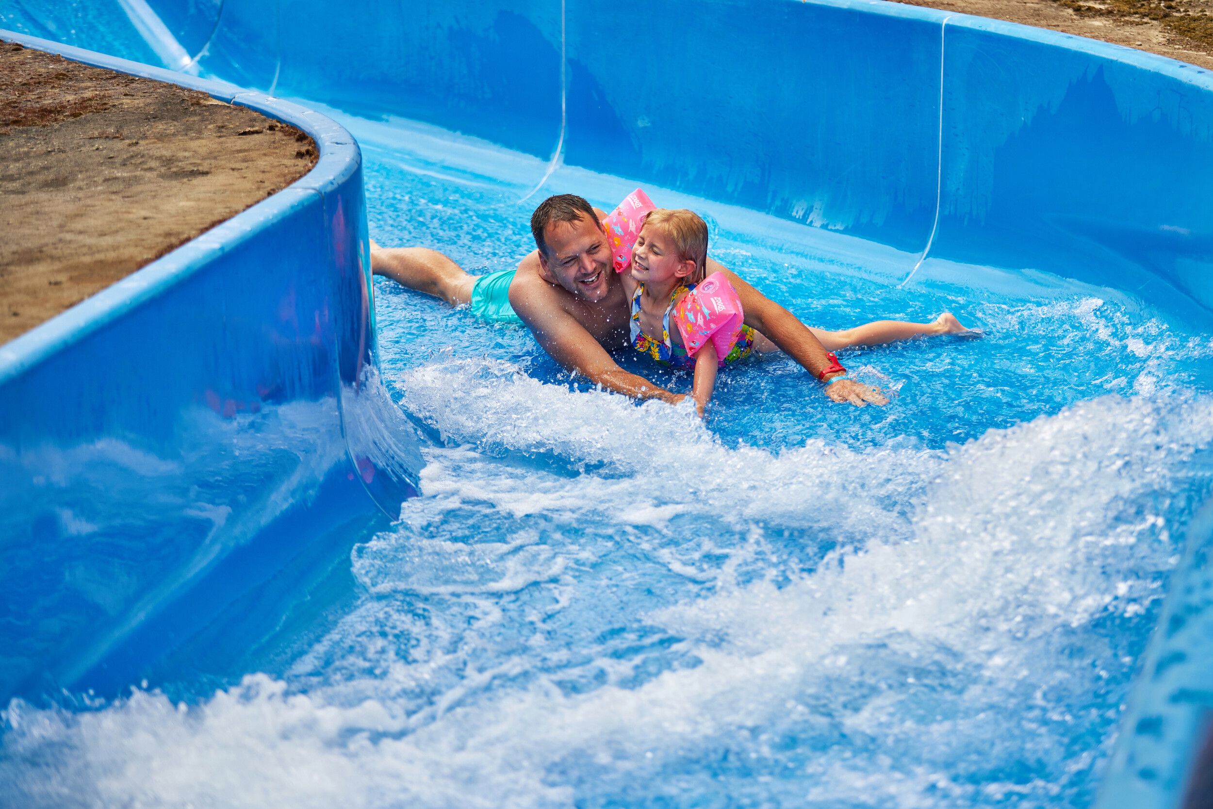 A father and his daughter going down a blue water slide.