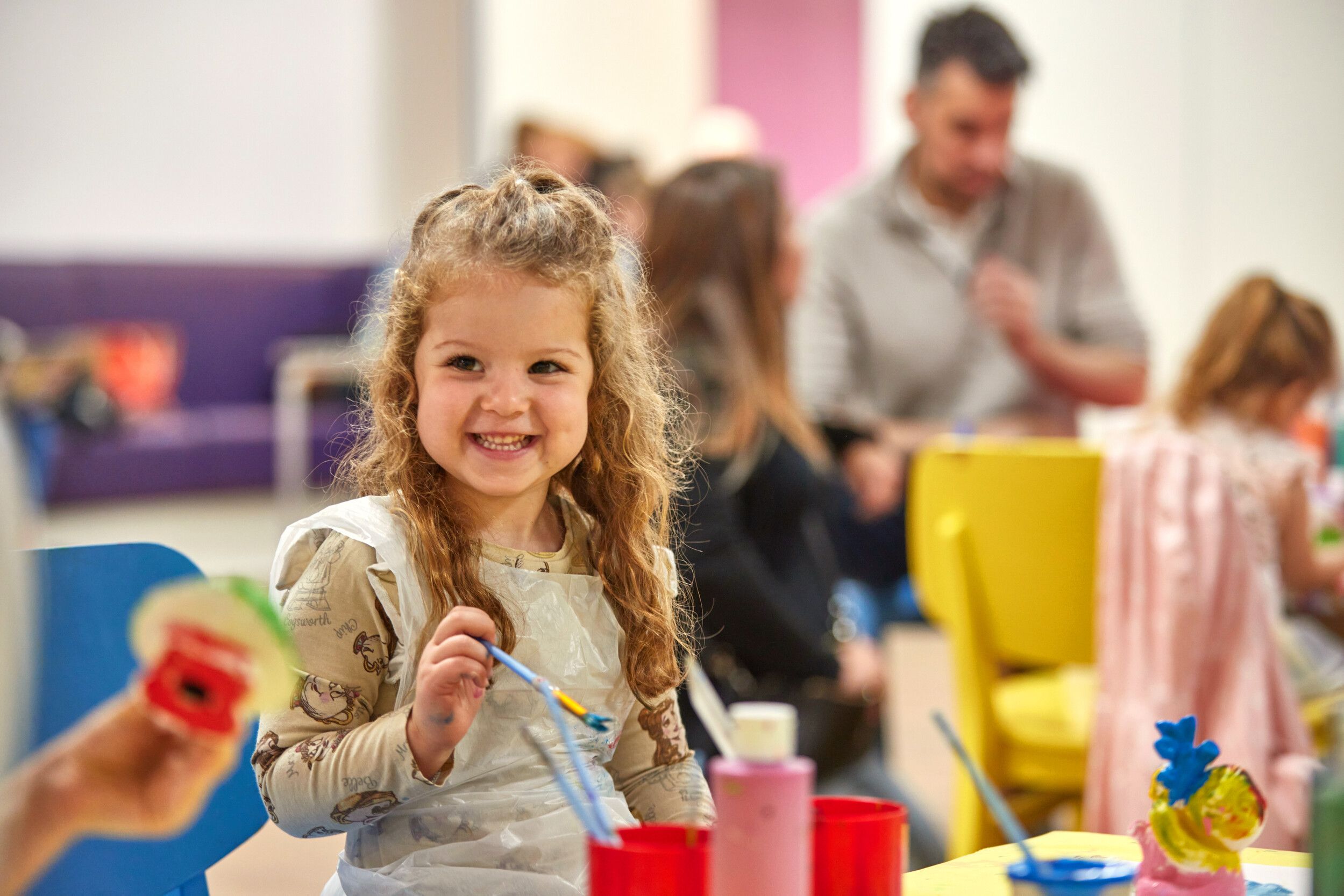 A little girl smiling while holding a paint brush.