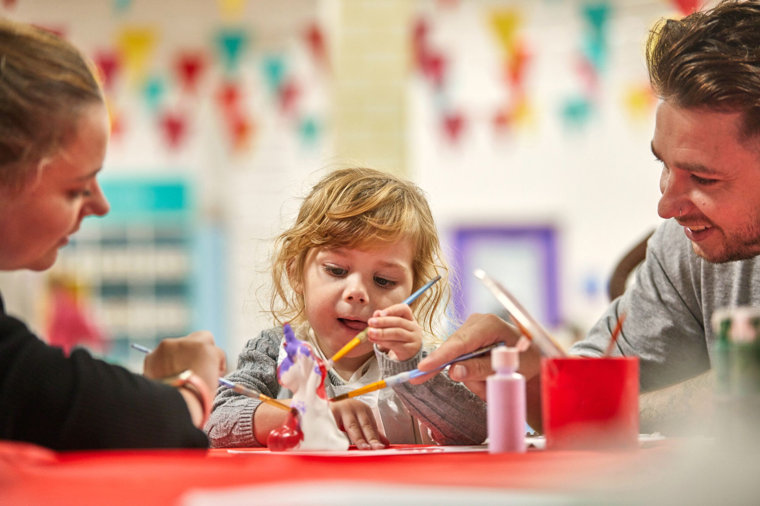 A little girl doing pottery painting along with her parents.