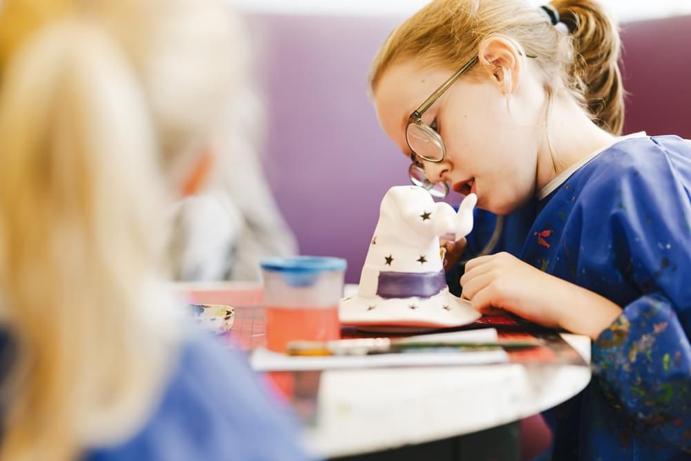 A young girl focused on painting her pottery.