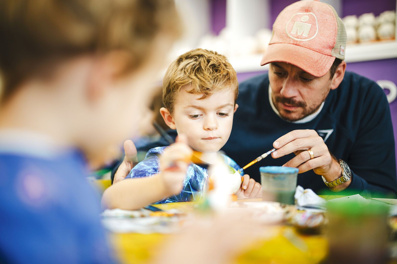 A young boy paints pottery with help from his father.