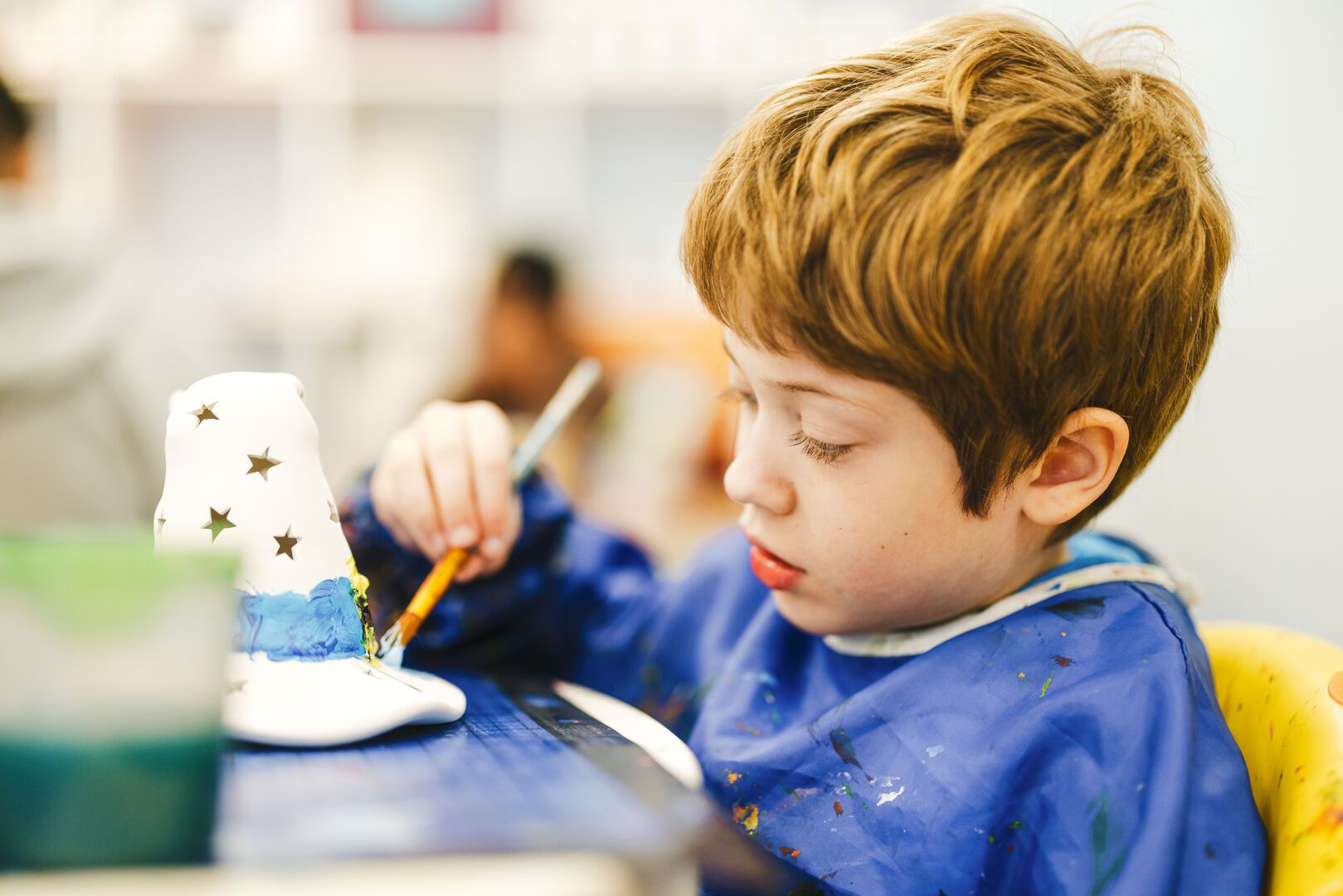 A young boy focused on painting his pottery.
