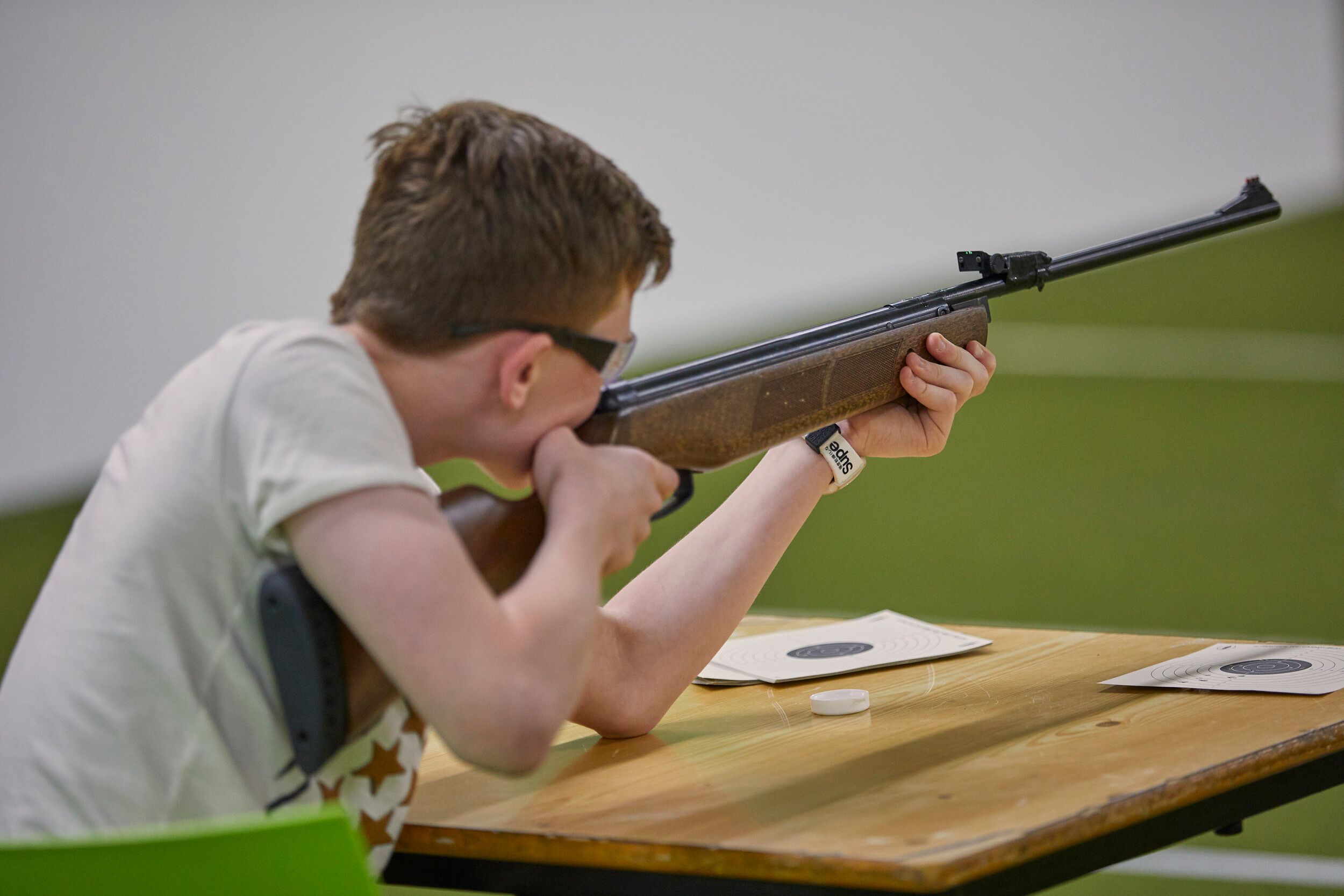A boy wearing protective glasses, holding a rifle while aiming at a target.