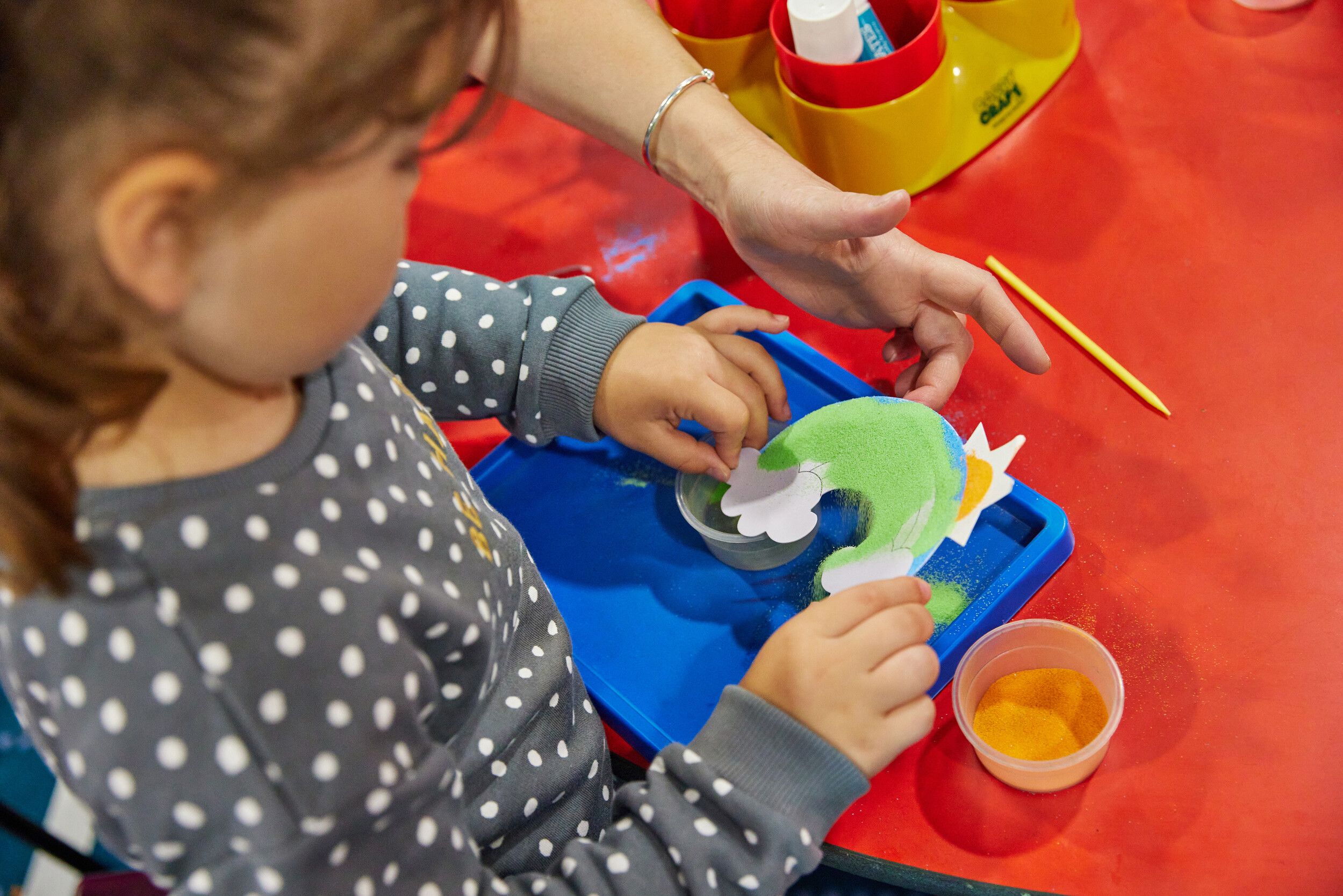 A little girl doing sand art using different colours.