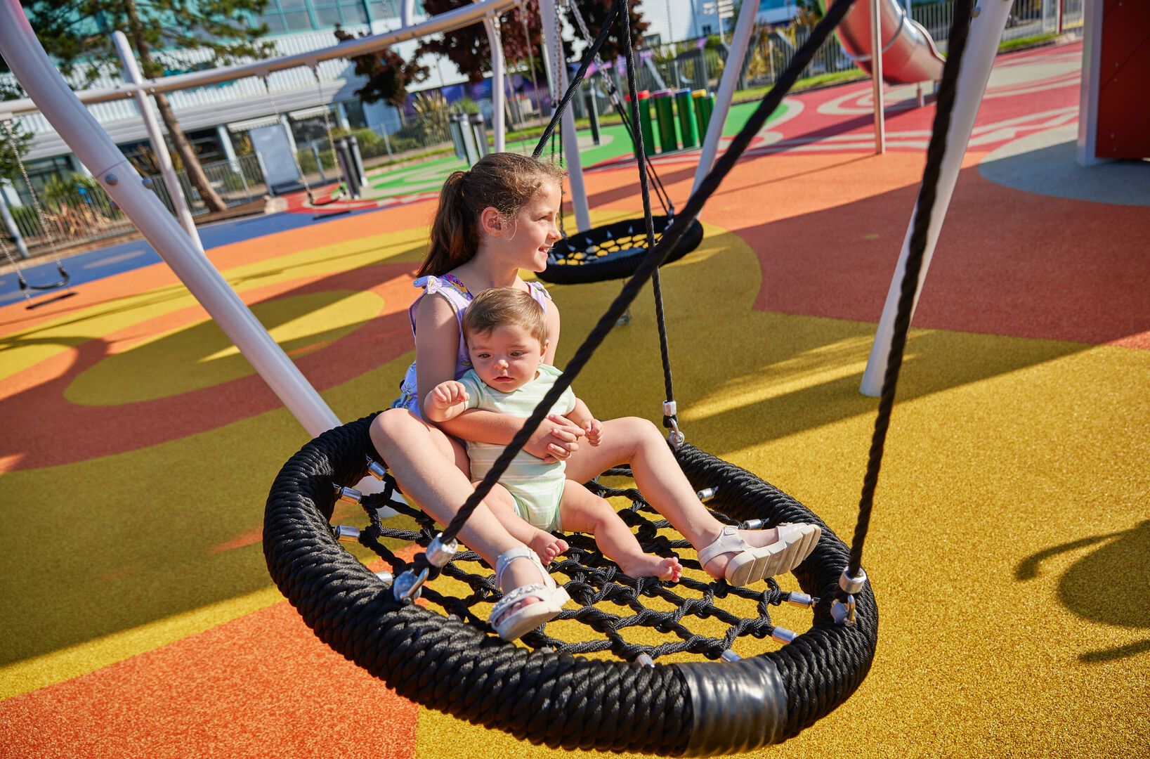 A young girl with her brother play together on a swing.