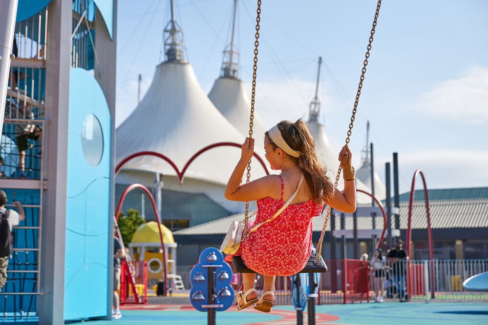 A young girl on a swing with the Skyline Pavilion in the background.
