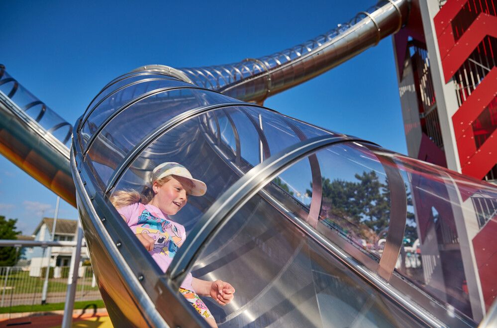 A young girl goes down the climbing tower slide.