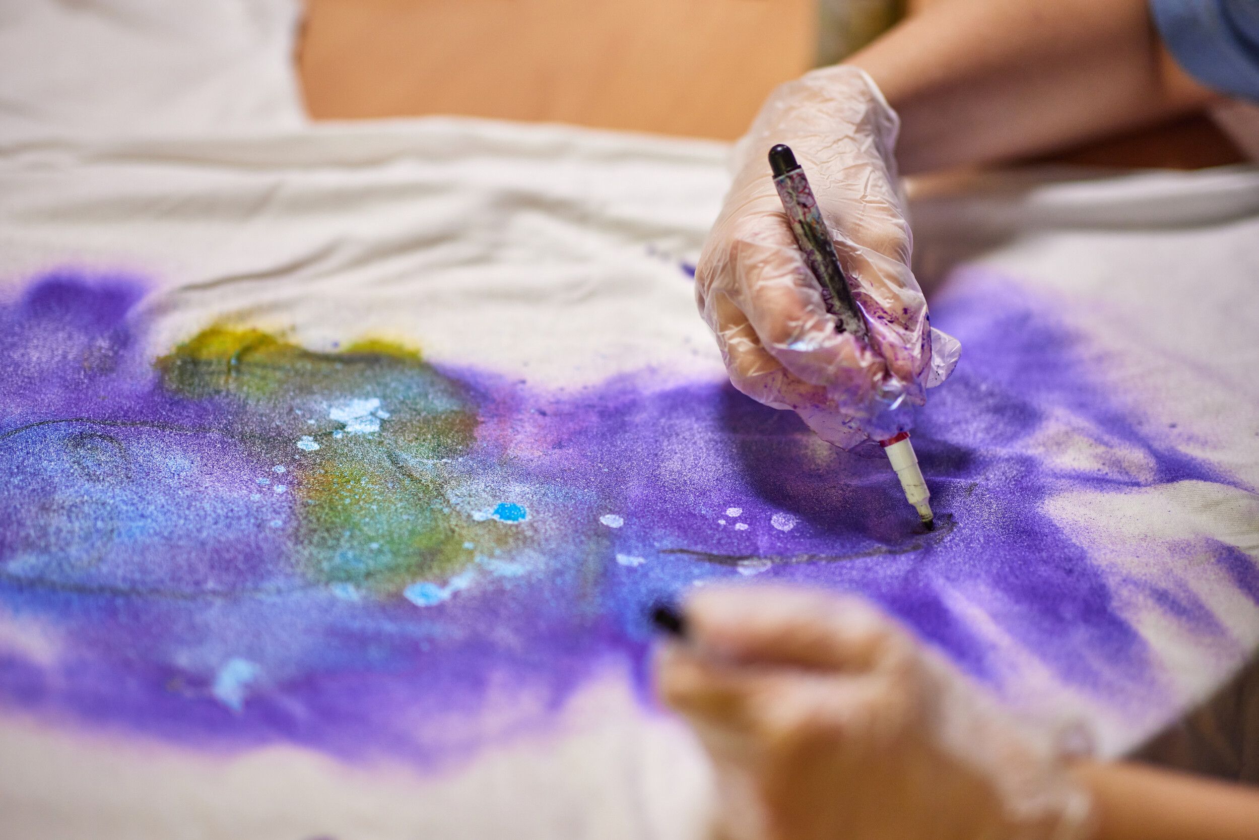A person wearing gloves carefully designing a shirt with violet paint.