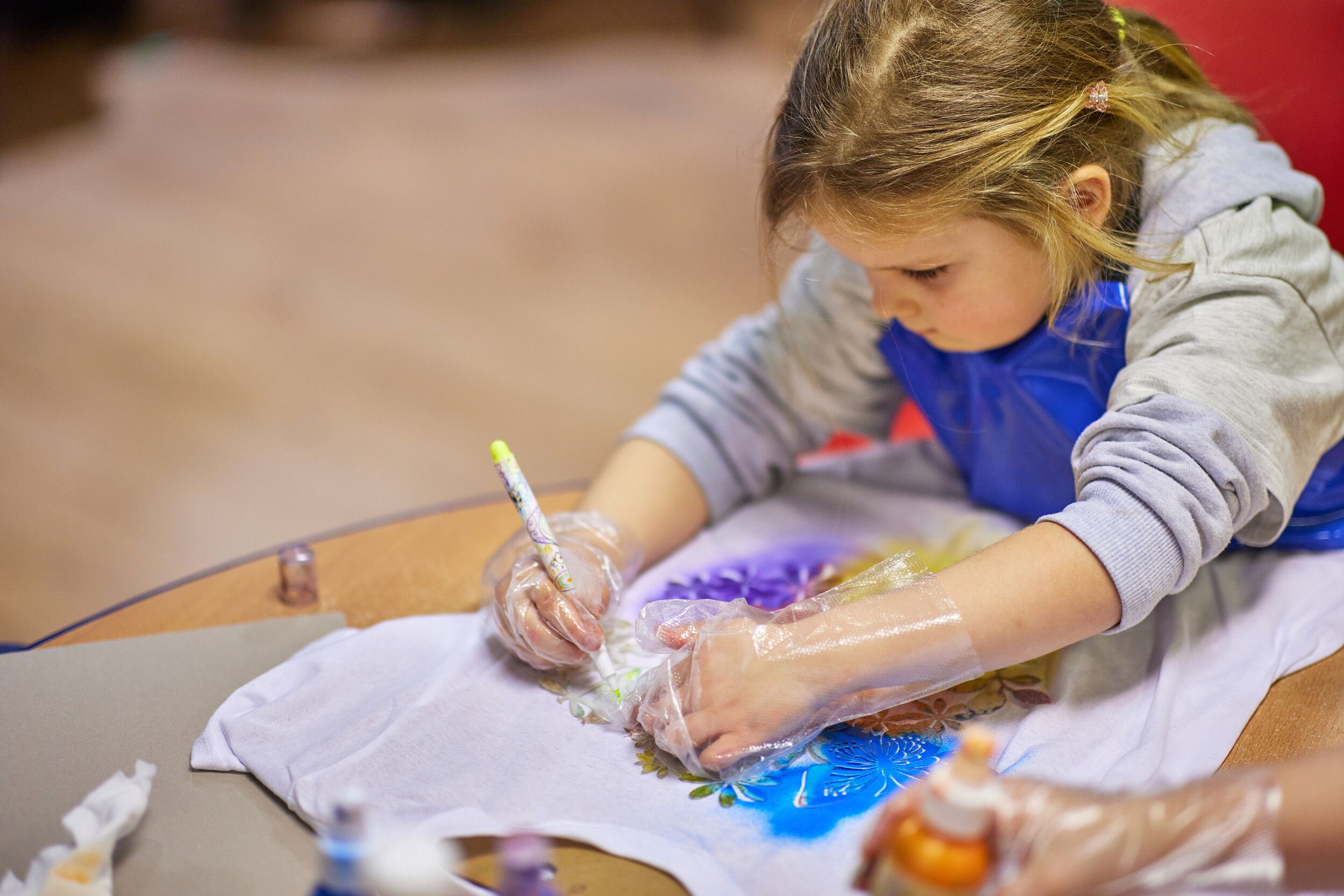 A little girl wearing plastic gloves designing a t-shirt. 