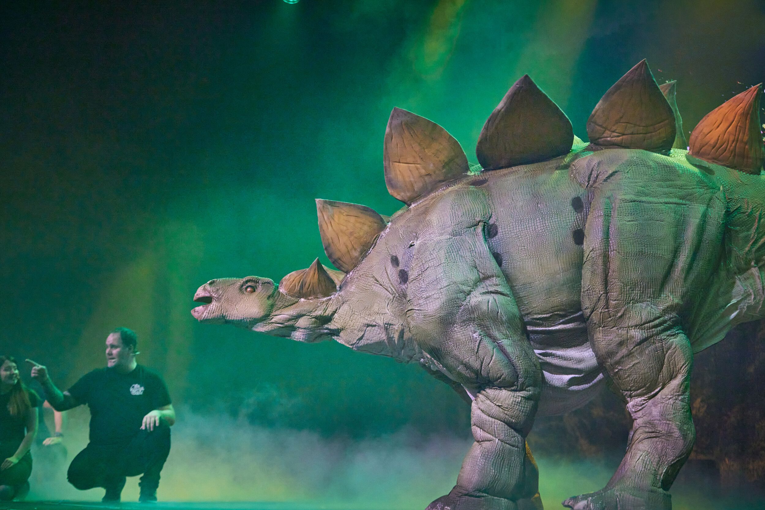 A life-size Stegosaurus beside two persons on stage.