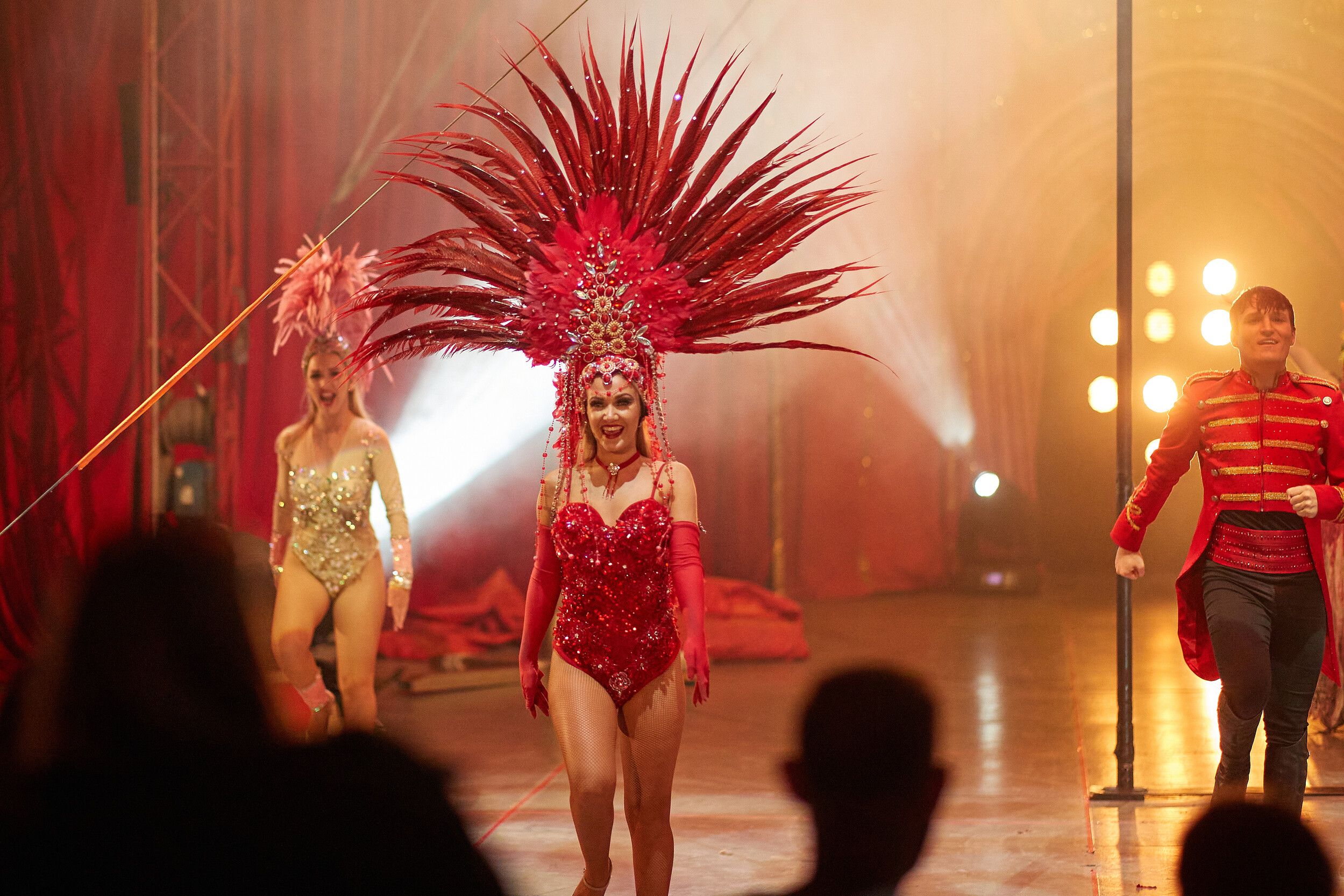 Three performers smiling, two are wearing colourful headdresses on stage.