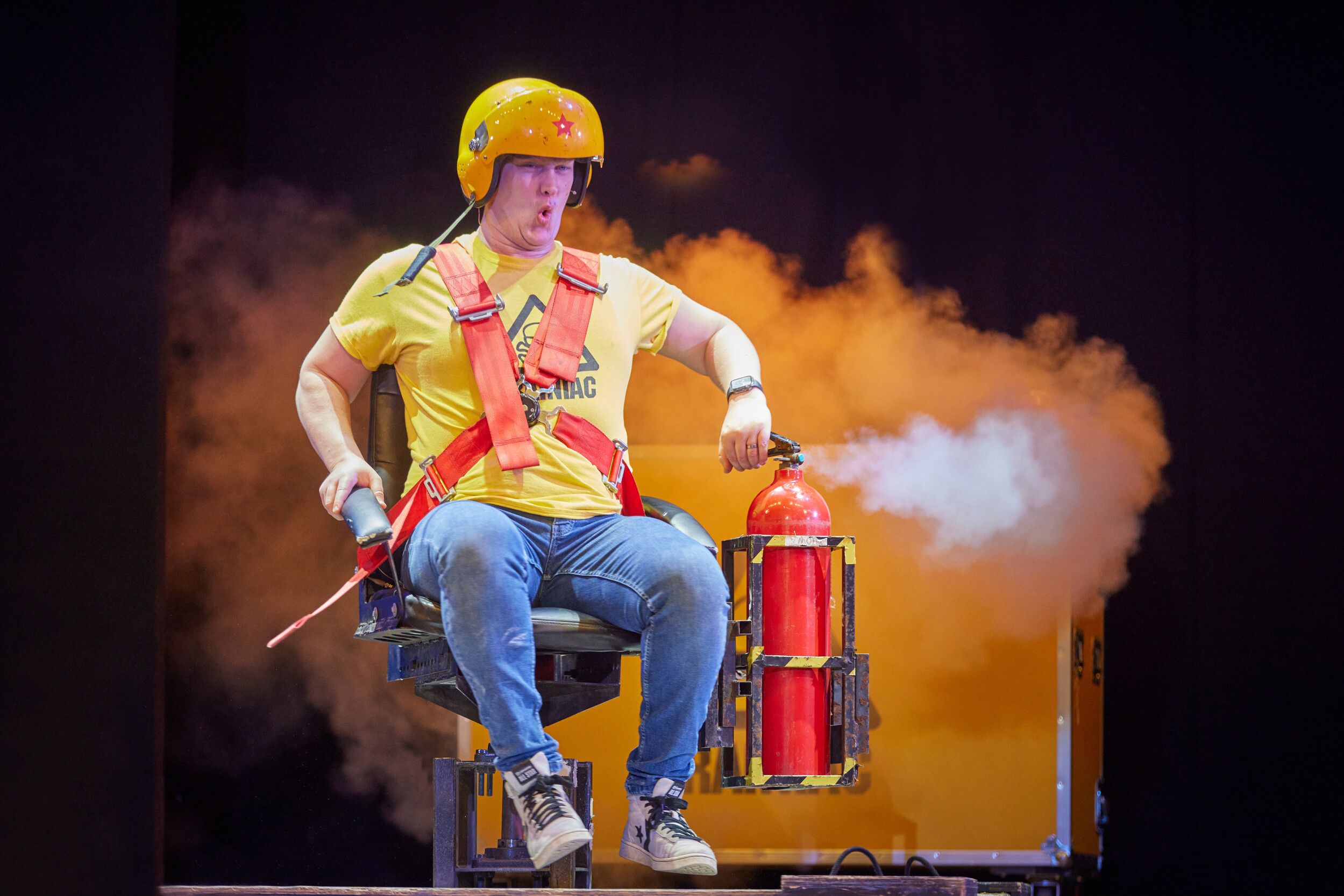A man sitting on a chair, wearing a helmet while using a fire extinguisher to spin around.