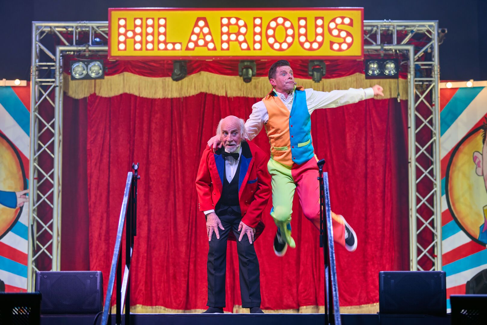 Danny Webb jumps into the air while on stage, and standing next to him is Clive Webb.