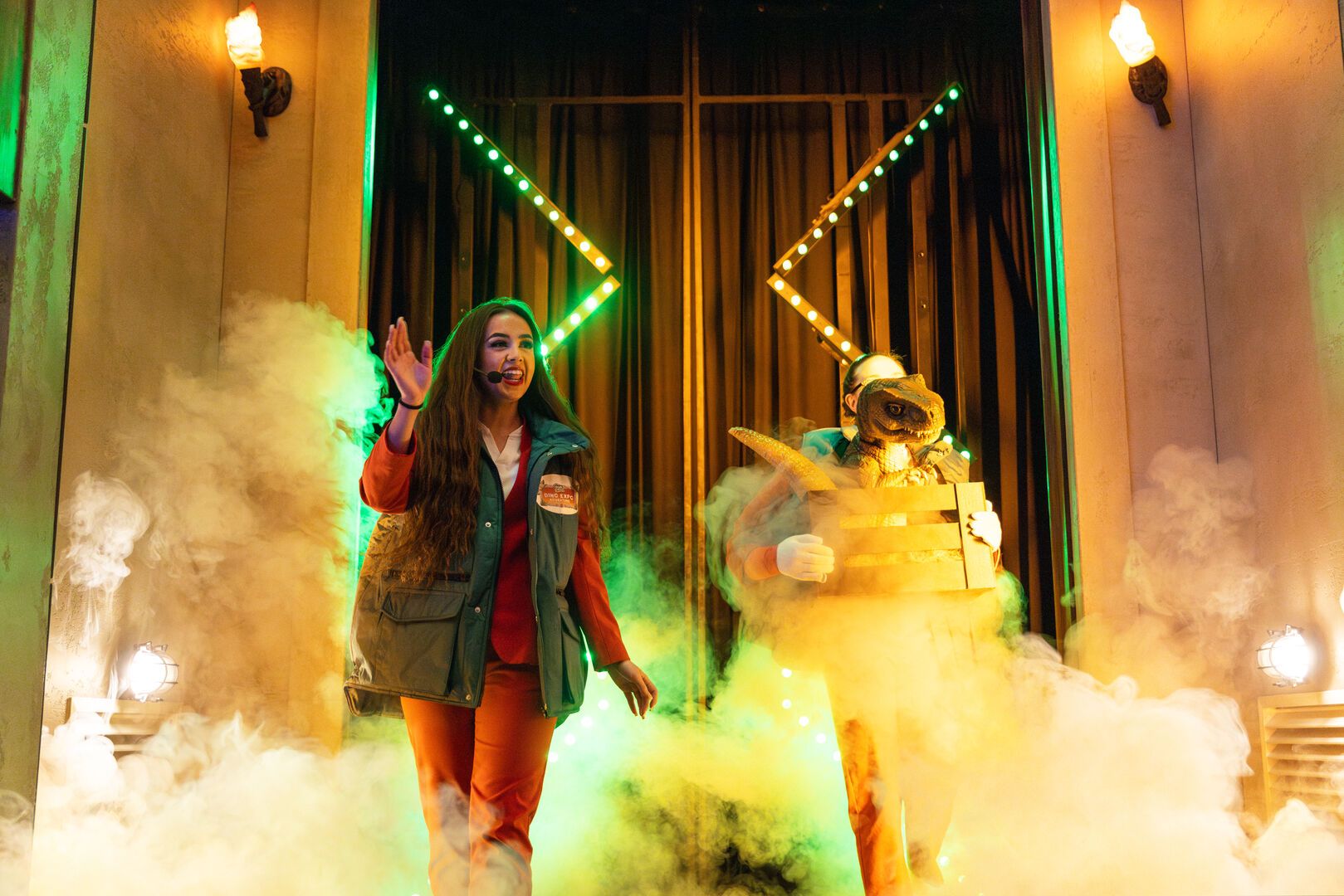 Two performers stand together in front of a smokey doorway as part of the Dino Expo exprience.