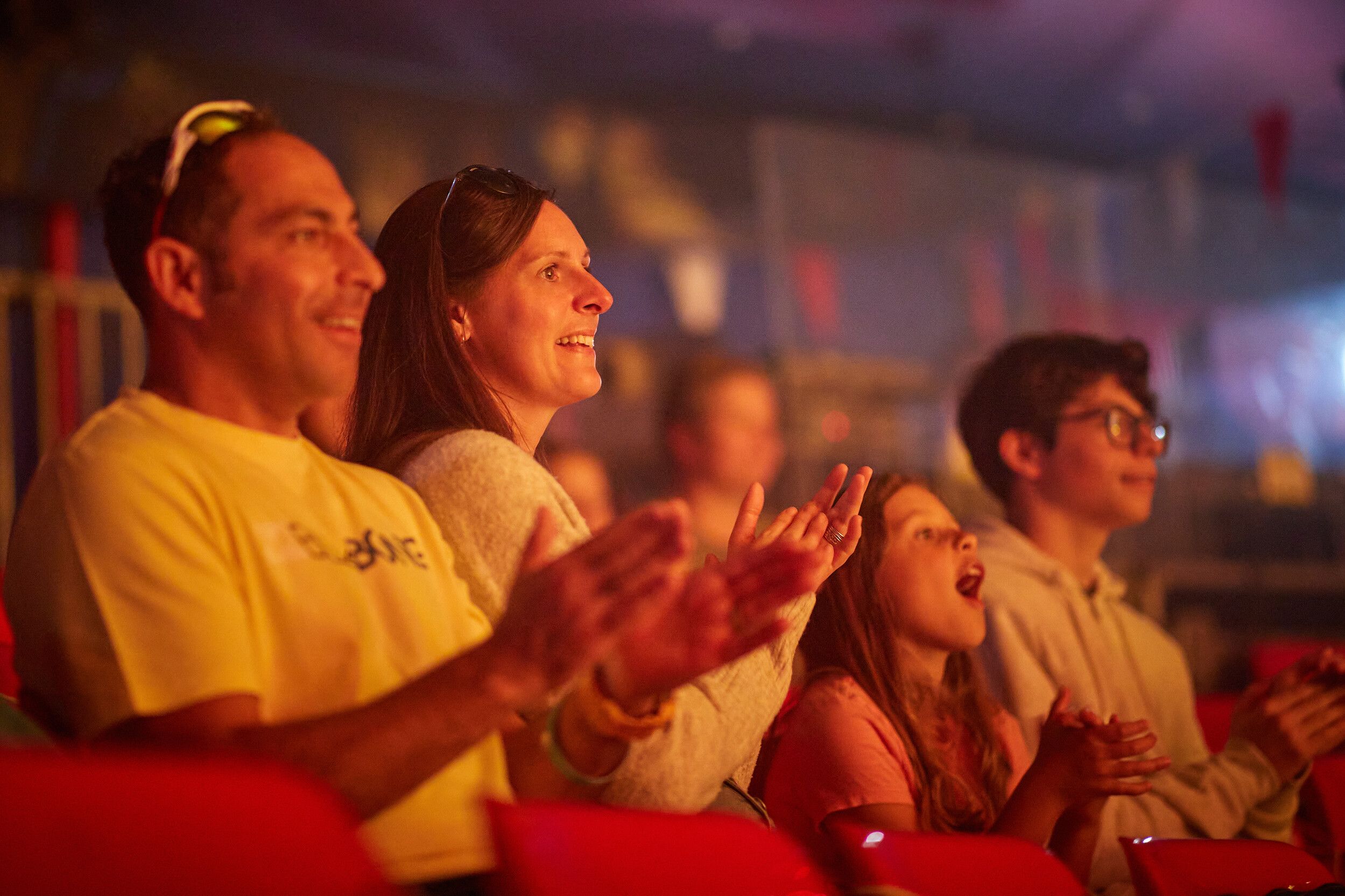 A family of four sitting down, clapping while watching a show.