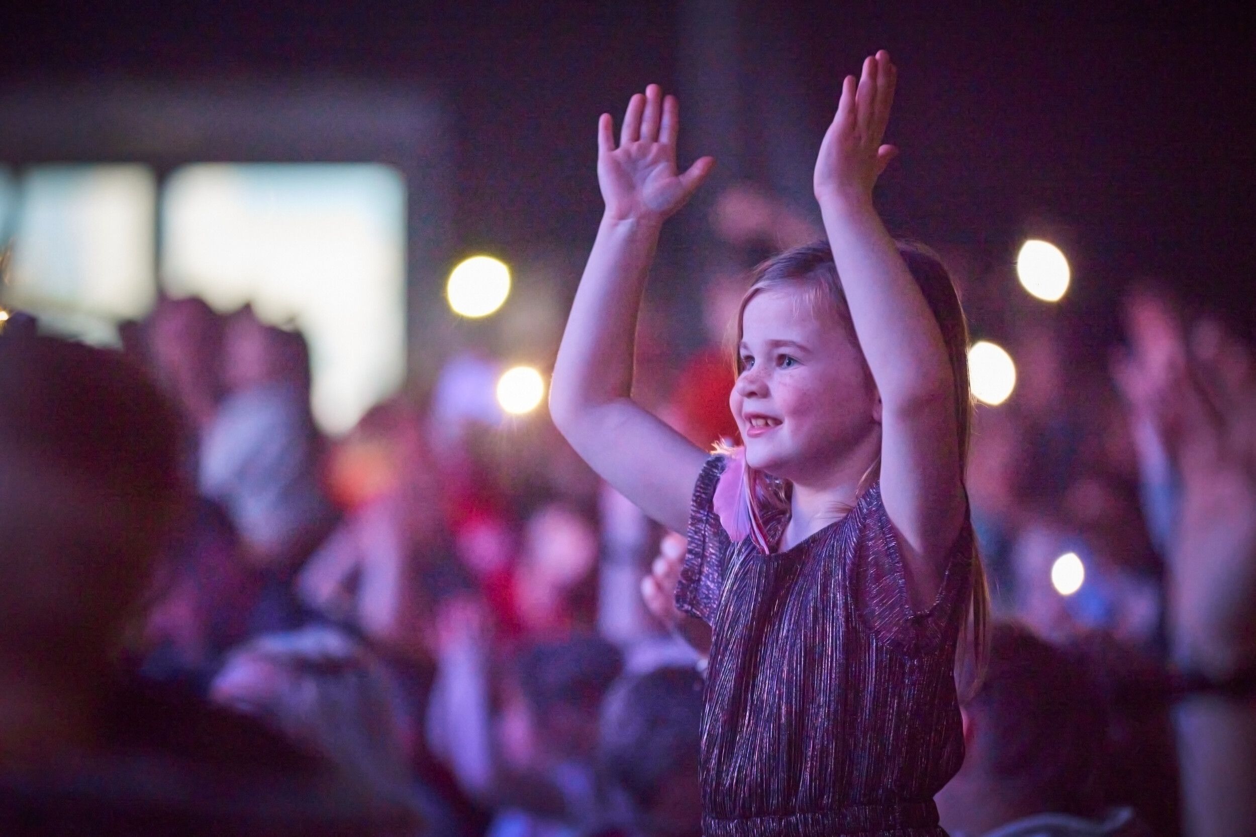 A little girl clapping her hands at the audience while watching a show.