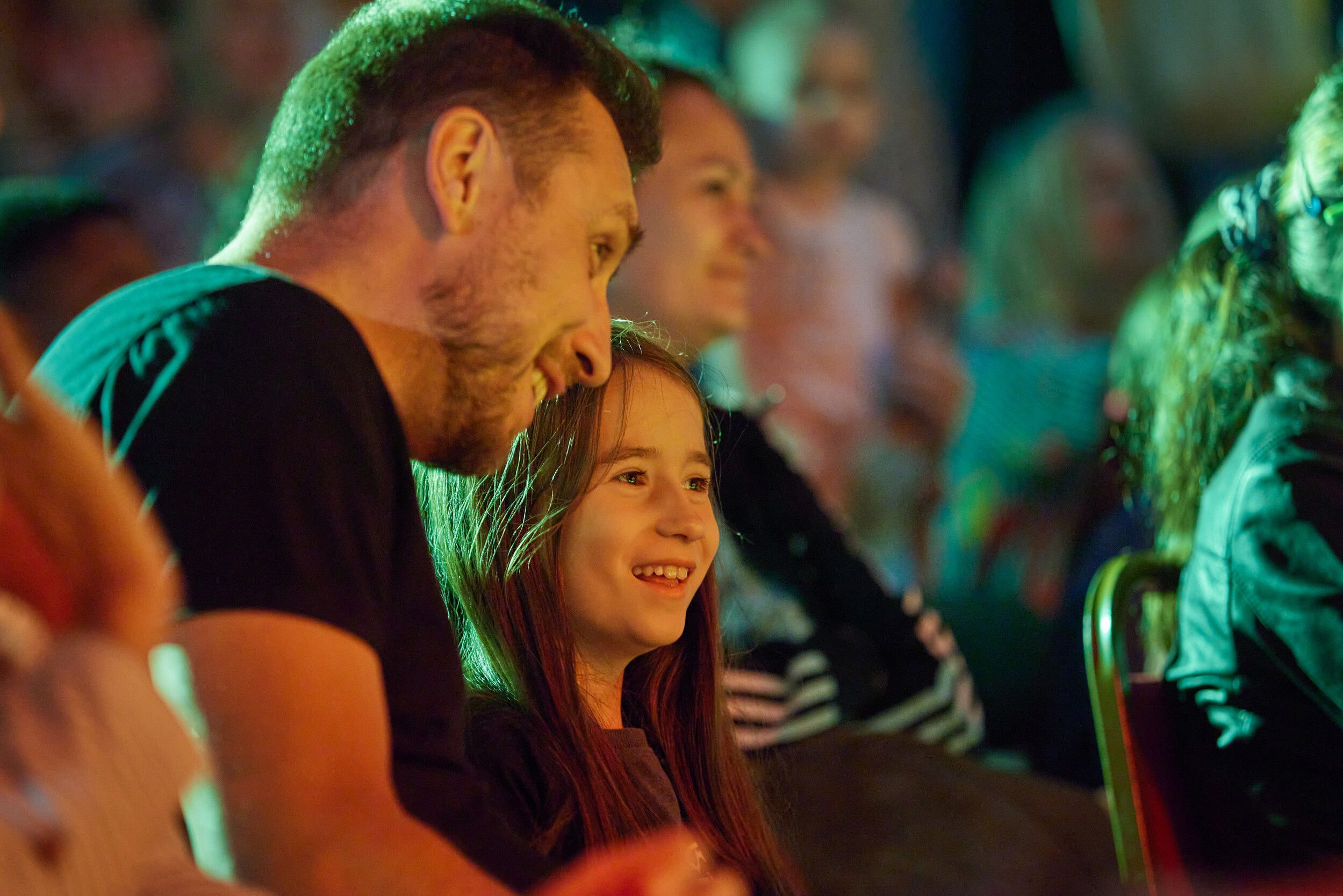 A father and his daughter sitting down at the audience while watching a show.