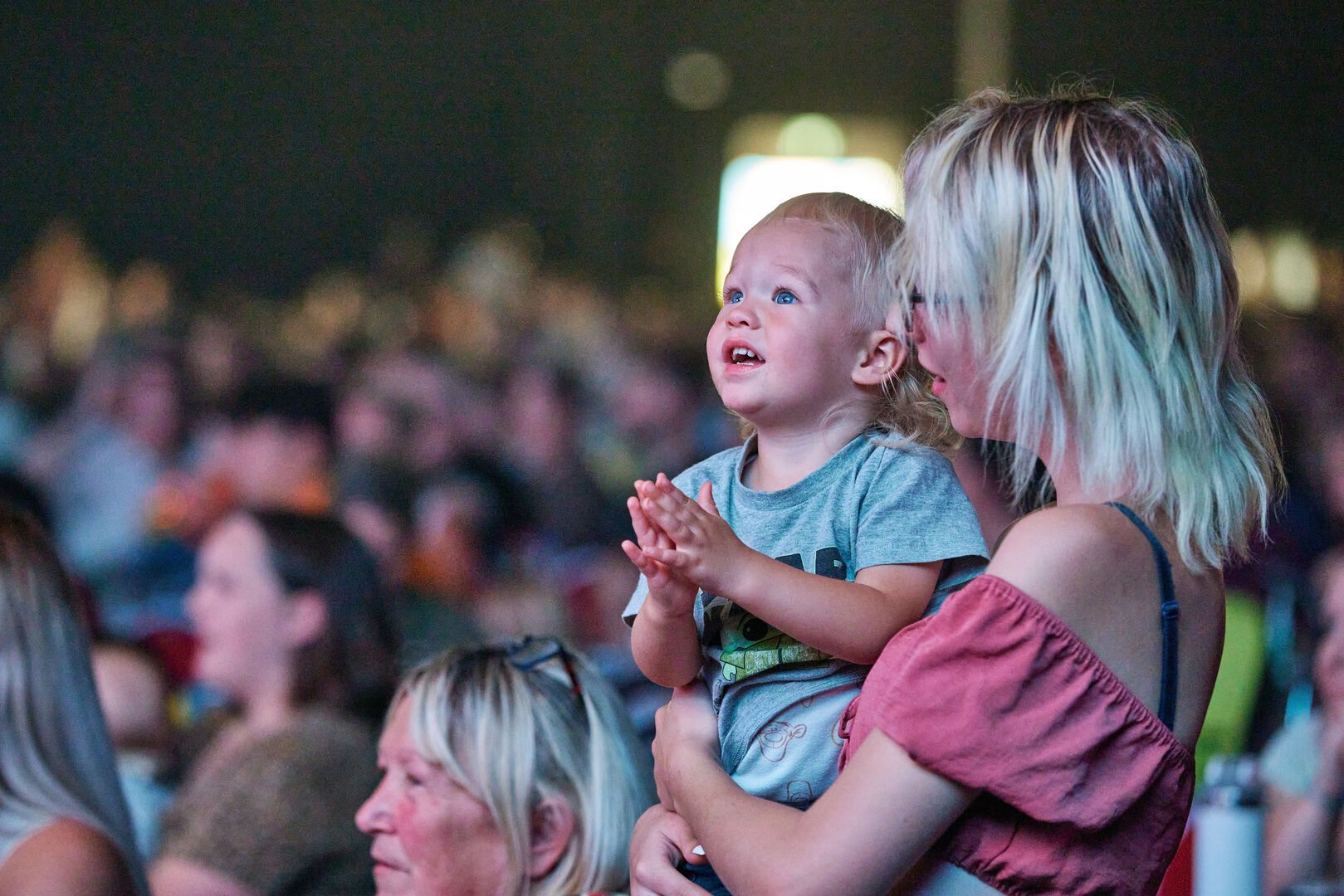 A mother hold her child while they stand in the audience together during a live show.