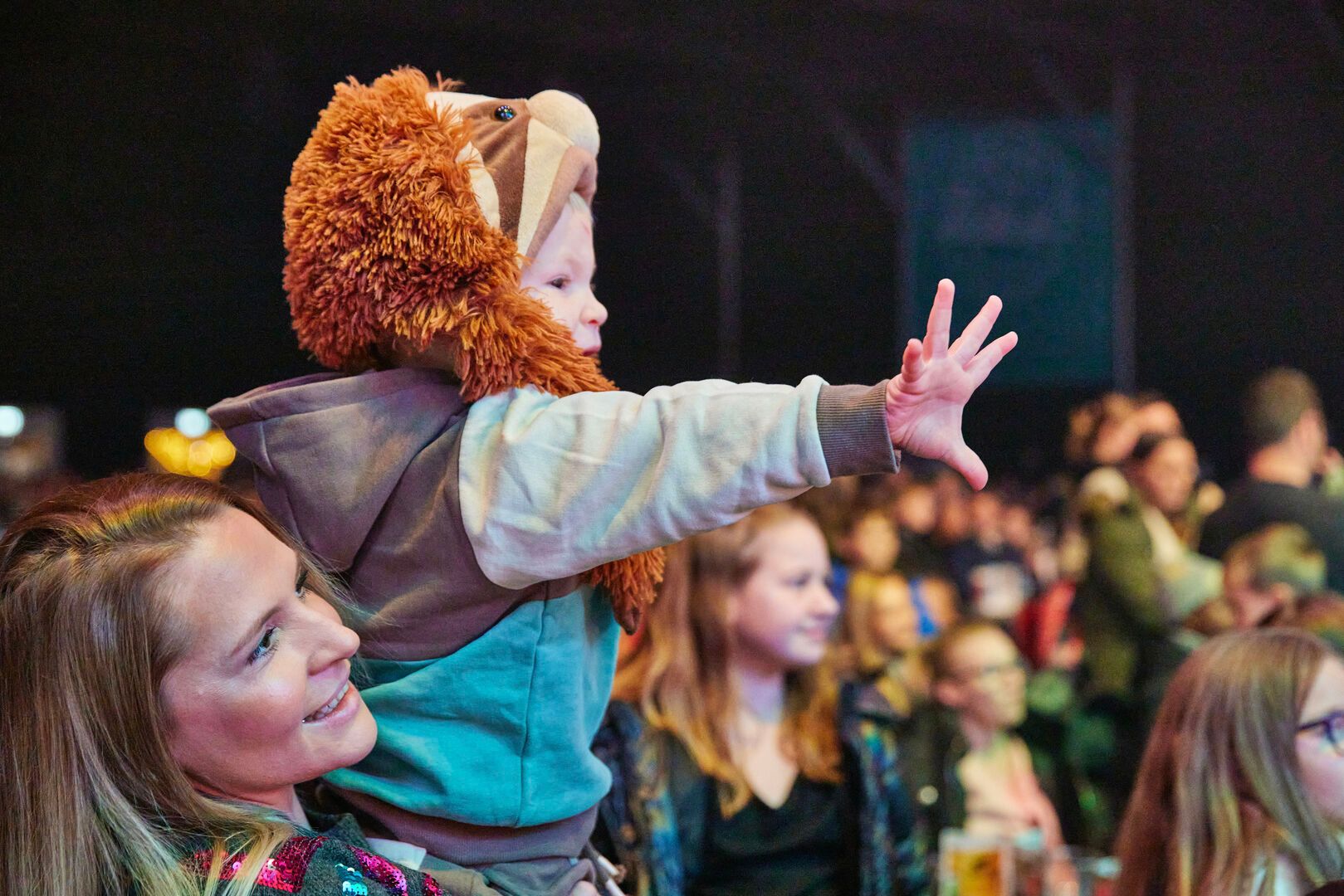 A young boy reaches out towards the stage while his mother holds him.