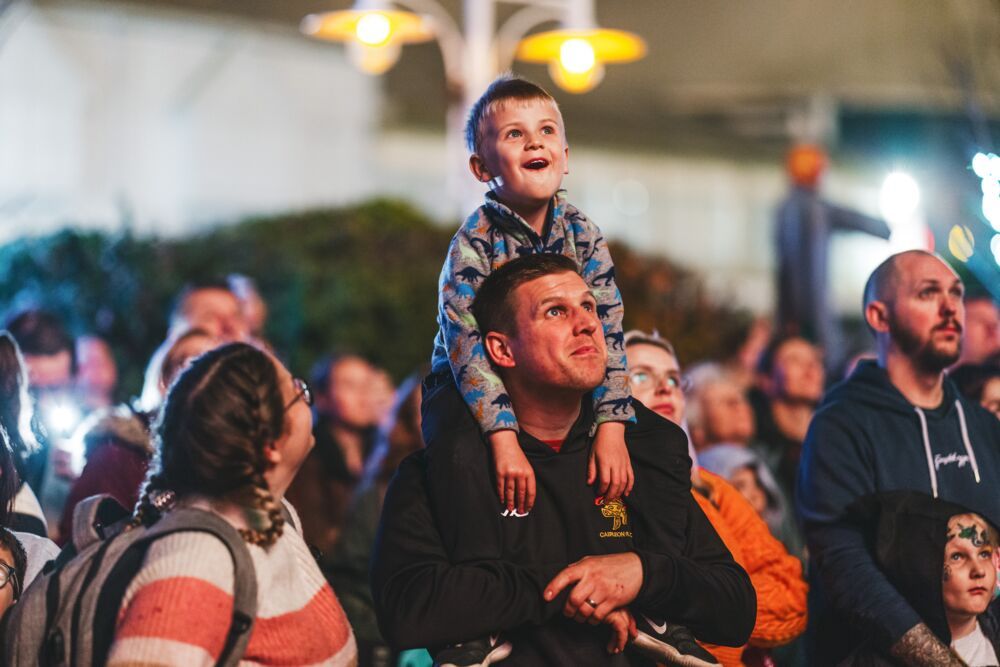A father carrying his son over his shoulder while watching a show.