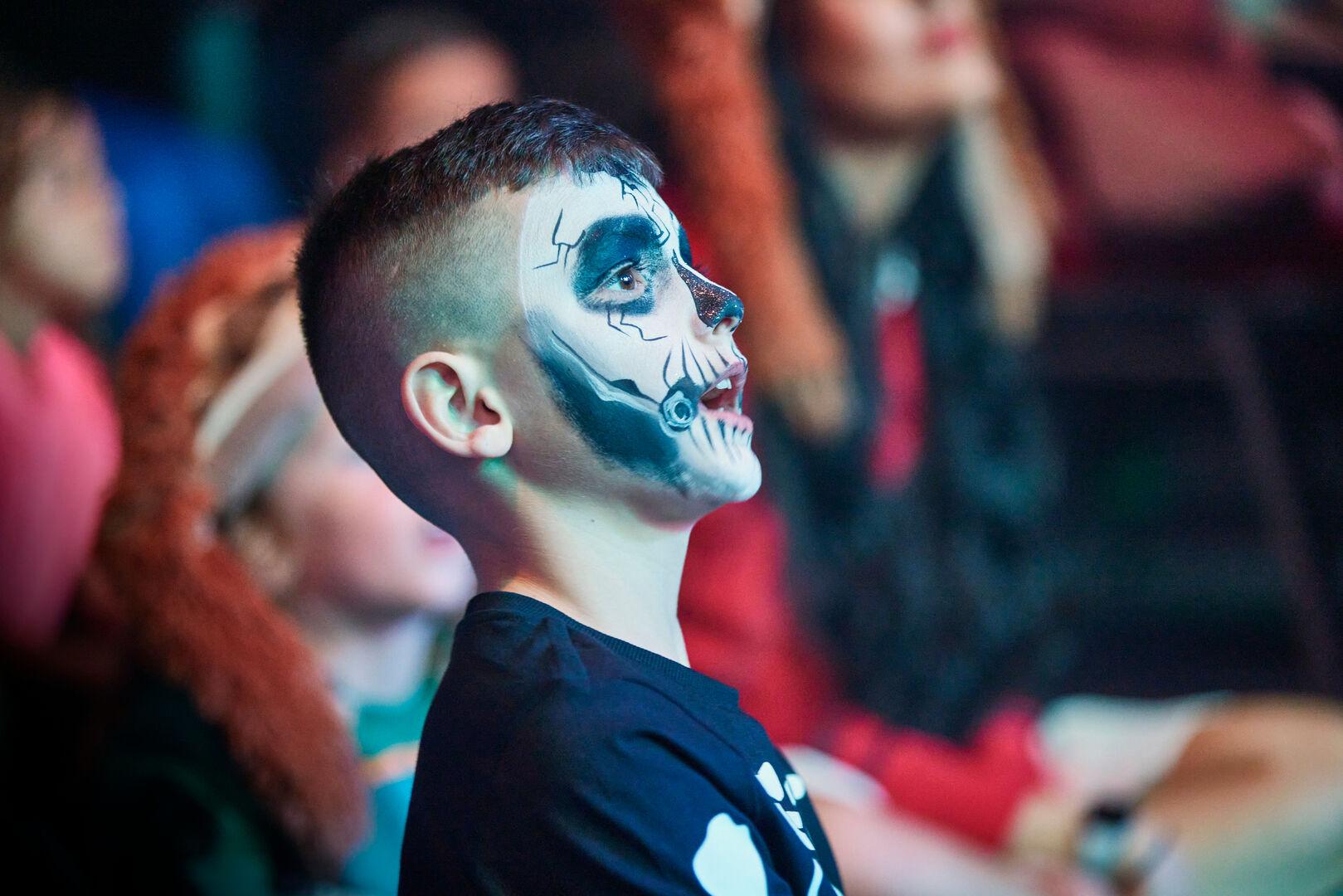 A little boy wearing a spooky face paint at the audience while watching a show.