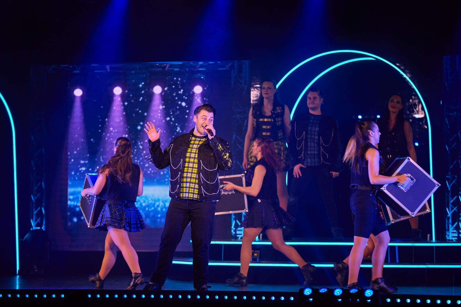 A performer holds one of his hands up as he sings into the microphone for a performance of ICONIC, at Butlin's.