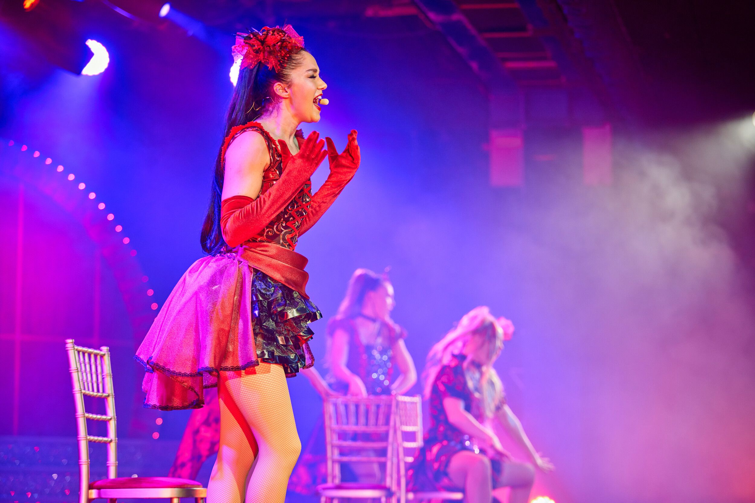 Three women wearing red outfits while singing on stage.