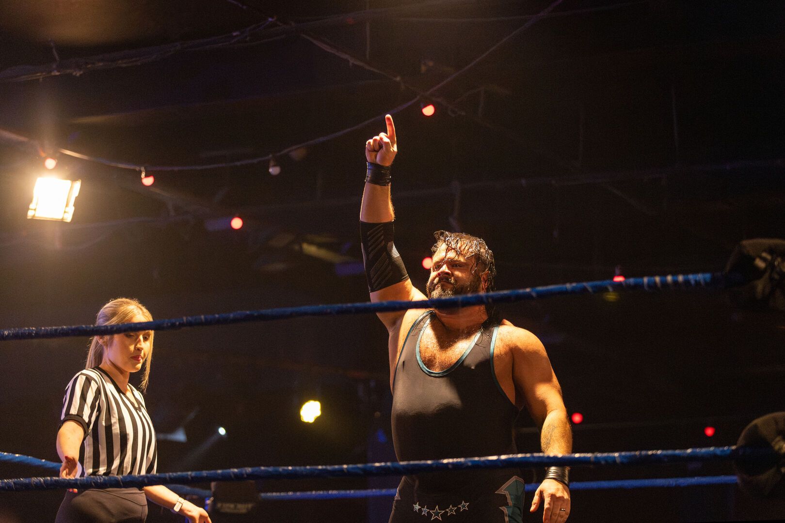A wrestler holds his hand the air and looks triumphant, the referee stands next to him.