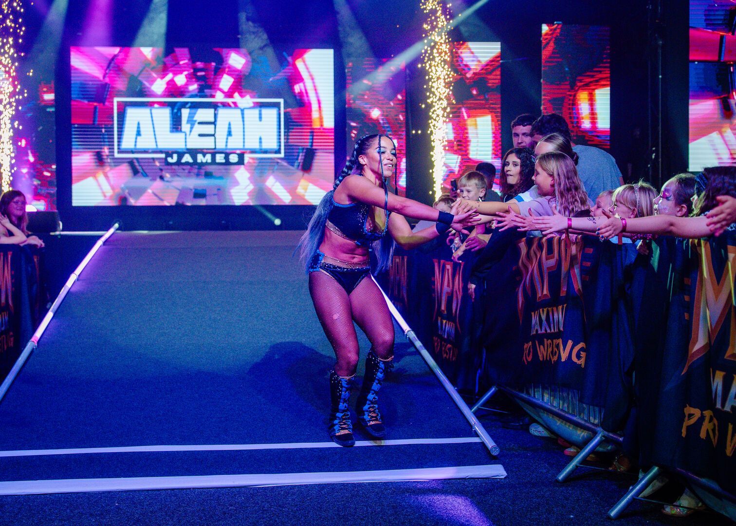 A wrestler greets the audience as she walks towards the ring during a Maximum Pro Wrestling performance at Butlin's.