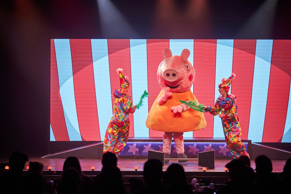 Two circus performers stand on either side of Peppa Pig.