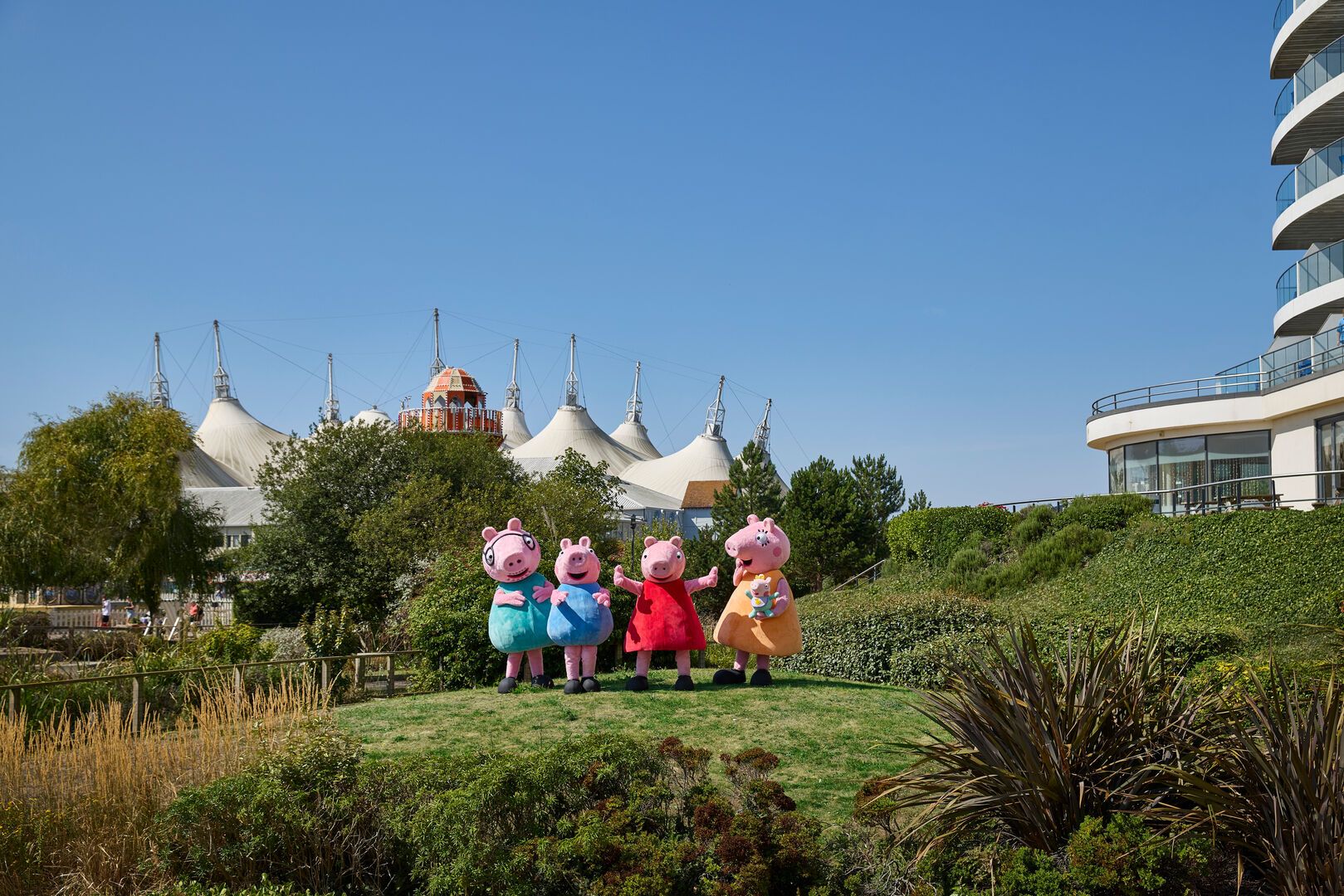 Peppa Pig and family pose for the camera at one of the Butlin's resorts, with the iconic Skyline Pavilion in the background.