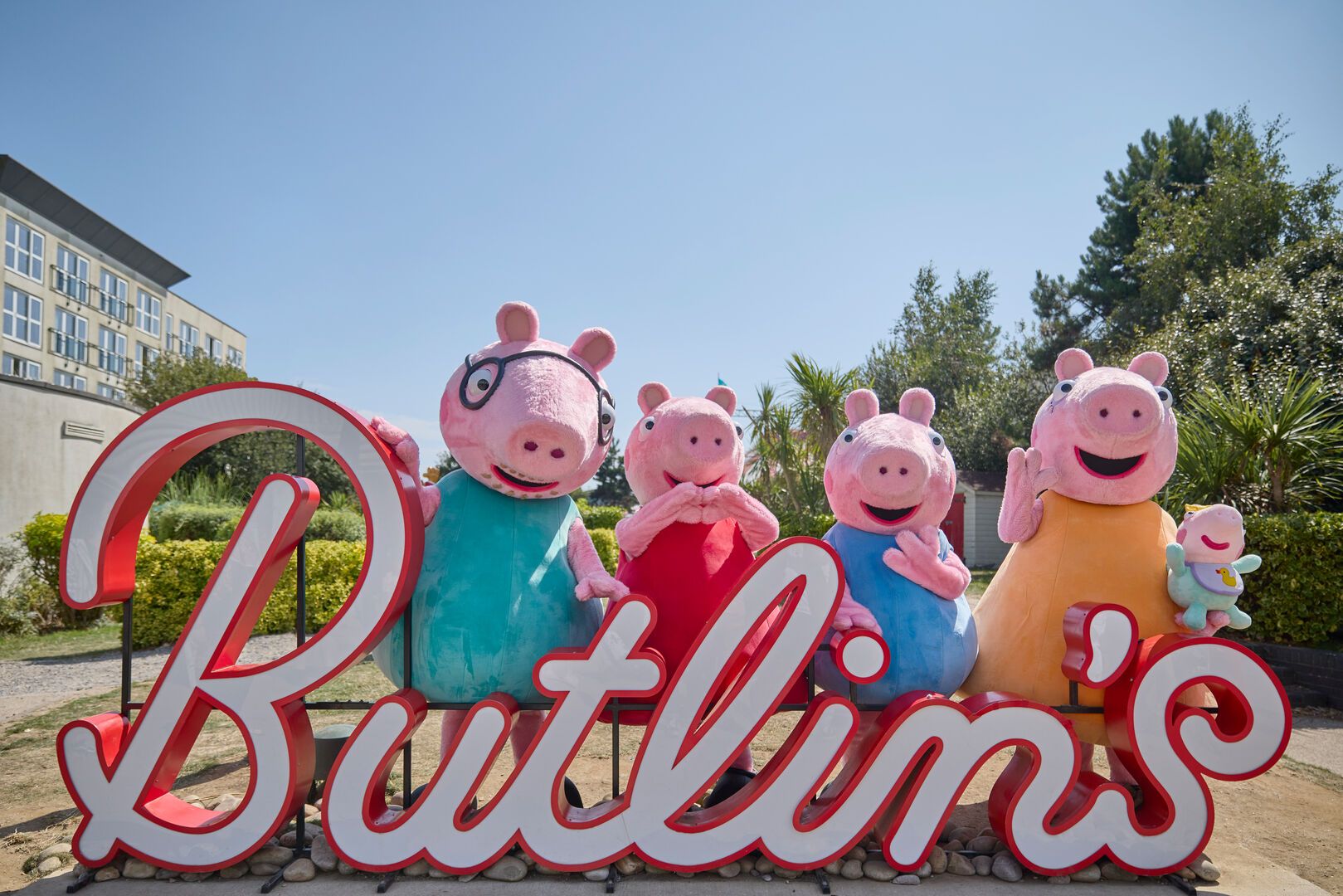 Peppa Pig and family pose for the camera in front of the neon Butlin's sign - Mummy Pig holds Evie in her arms.