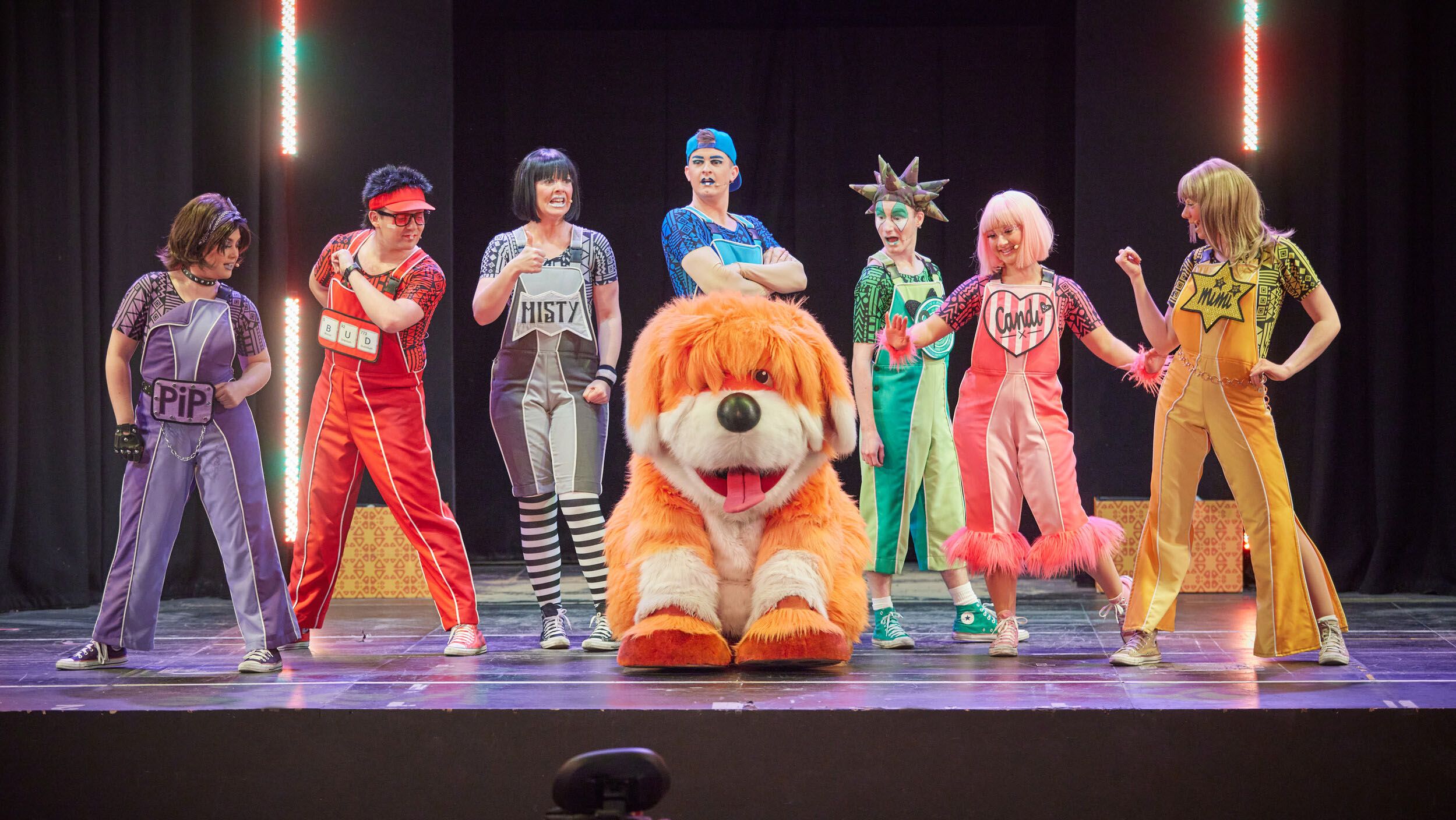 Skyline Gang members wearing colourful outfits performing behind Rainbow the dog on stage.