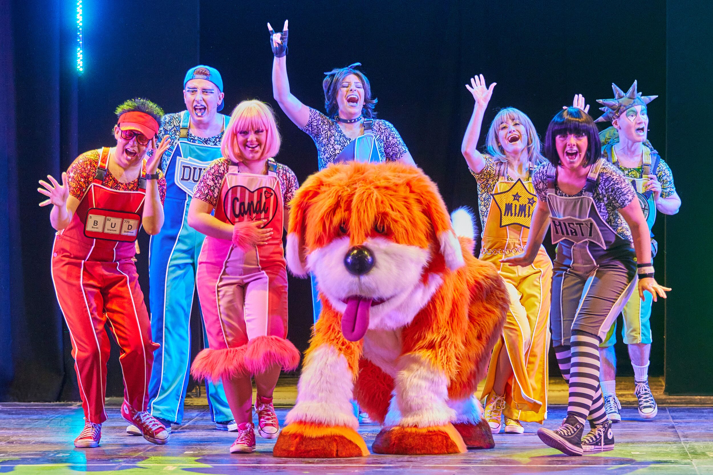 Skyline Gang members wearing colourful outfits while performing with Rainbow the dog on stage.