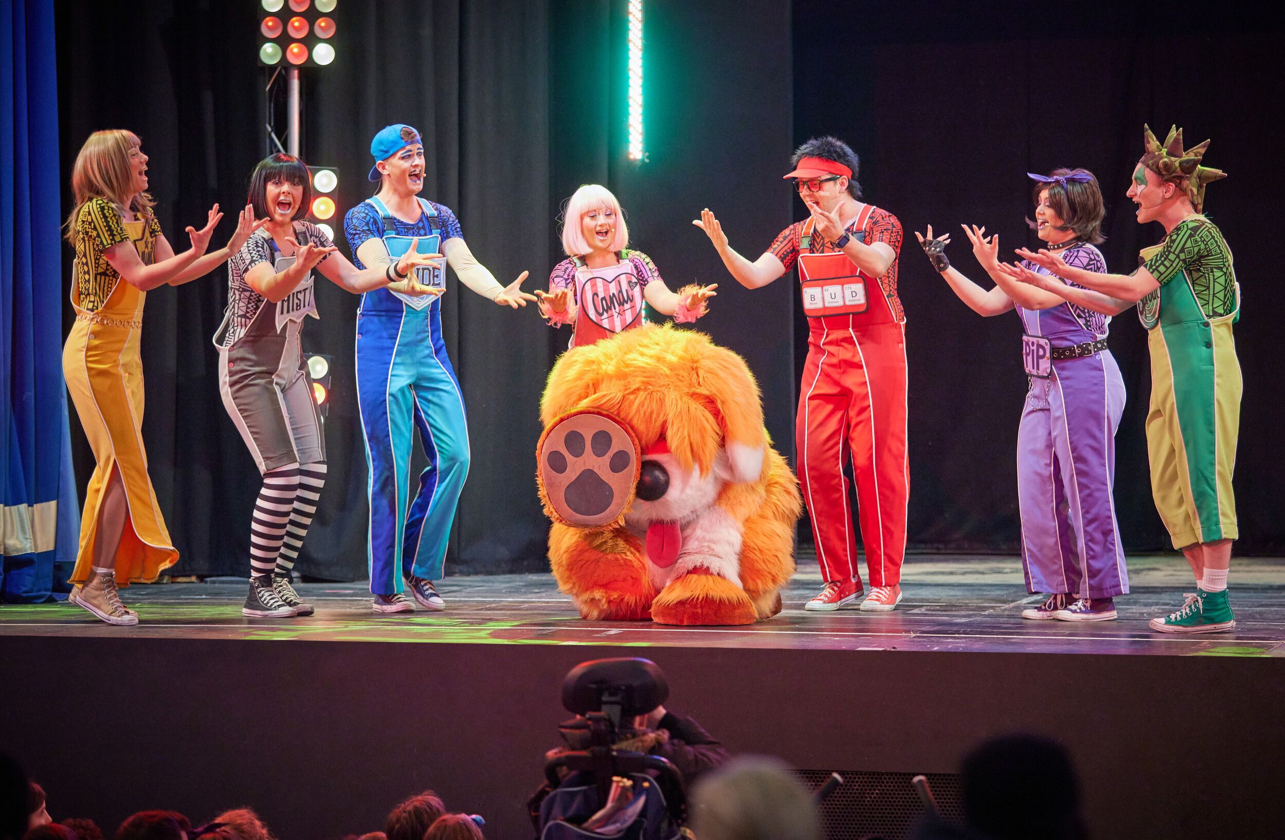 Skyline Gang members wearing colourful outfits performing behind Rainbow the dog on stage.