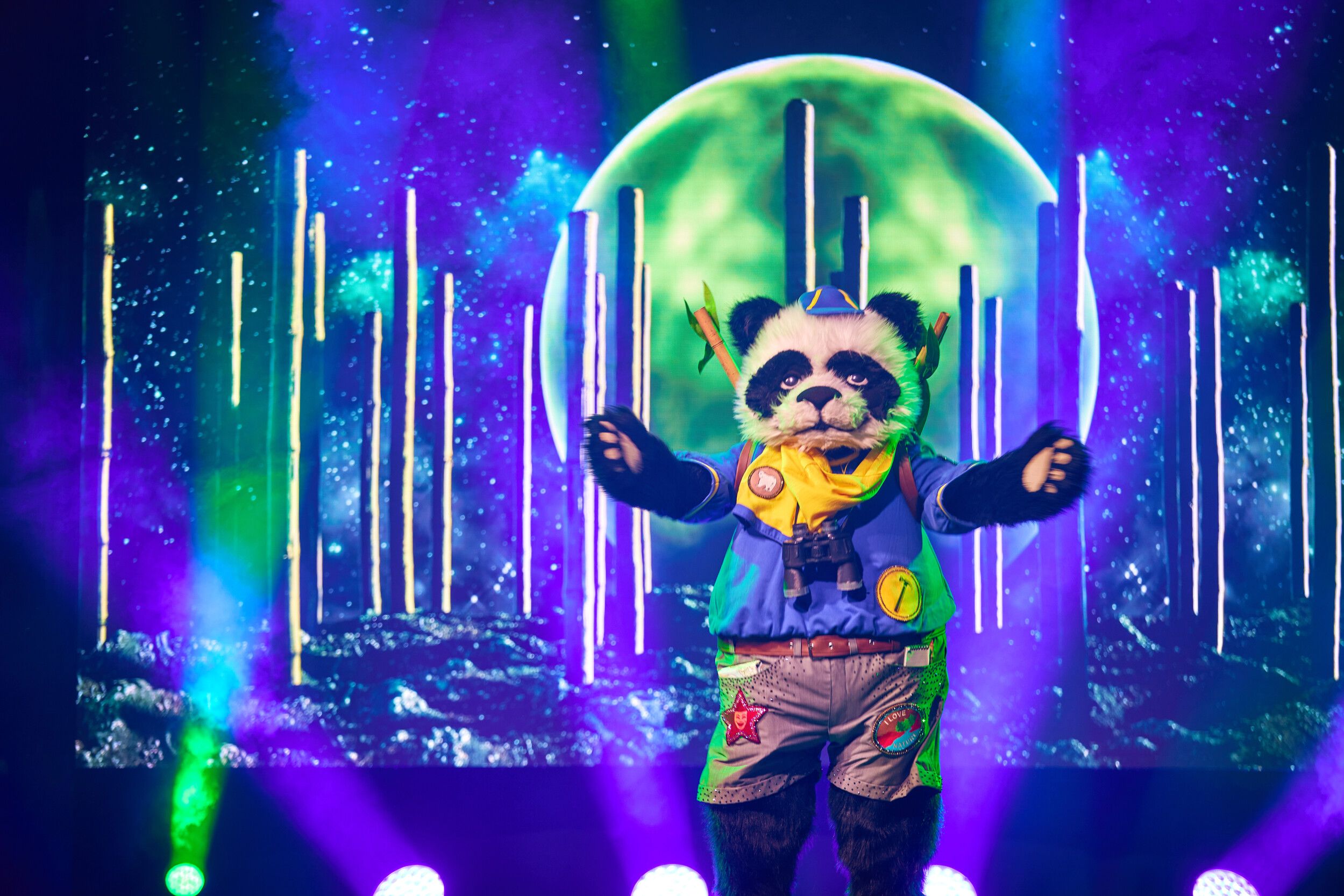 Panda performs on stage during a Masked Singer performance with its arms outstretched.