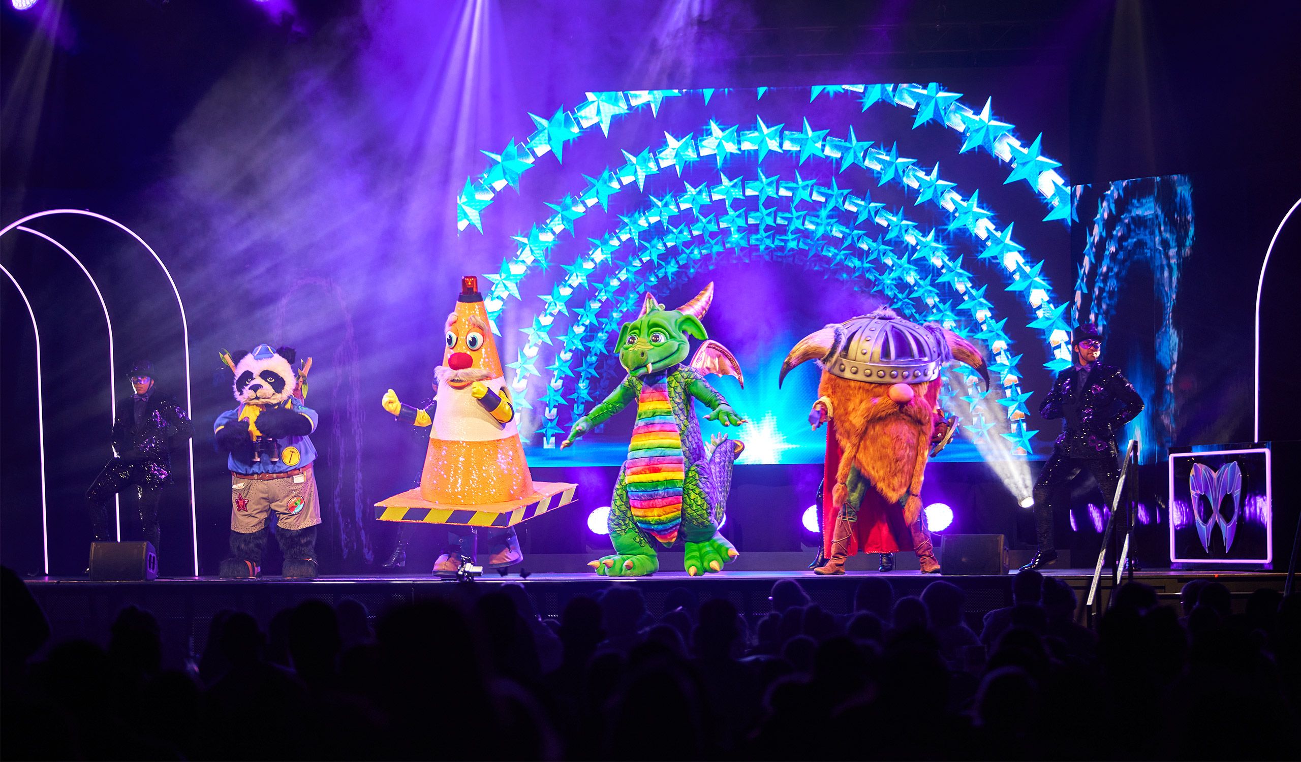 Four characters perform on stage together during a live performance of The Masked Singer.