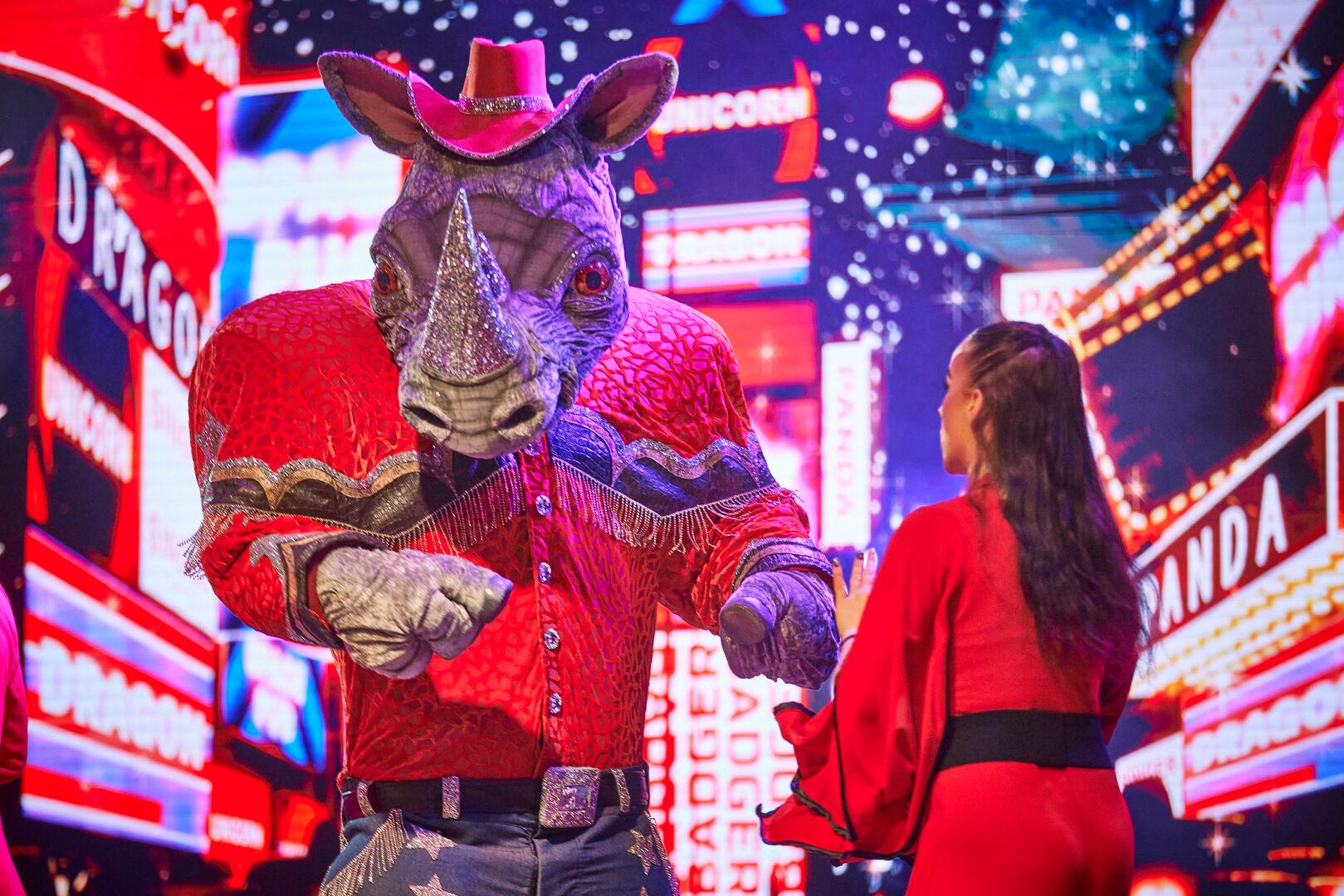 Rhino, a Masked Singer character, performs on stage with a woman in a red outfit.