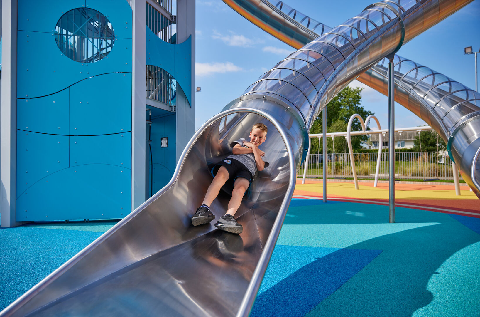 A young boy coming down one of the climbing tower slides.